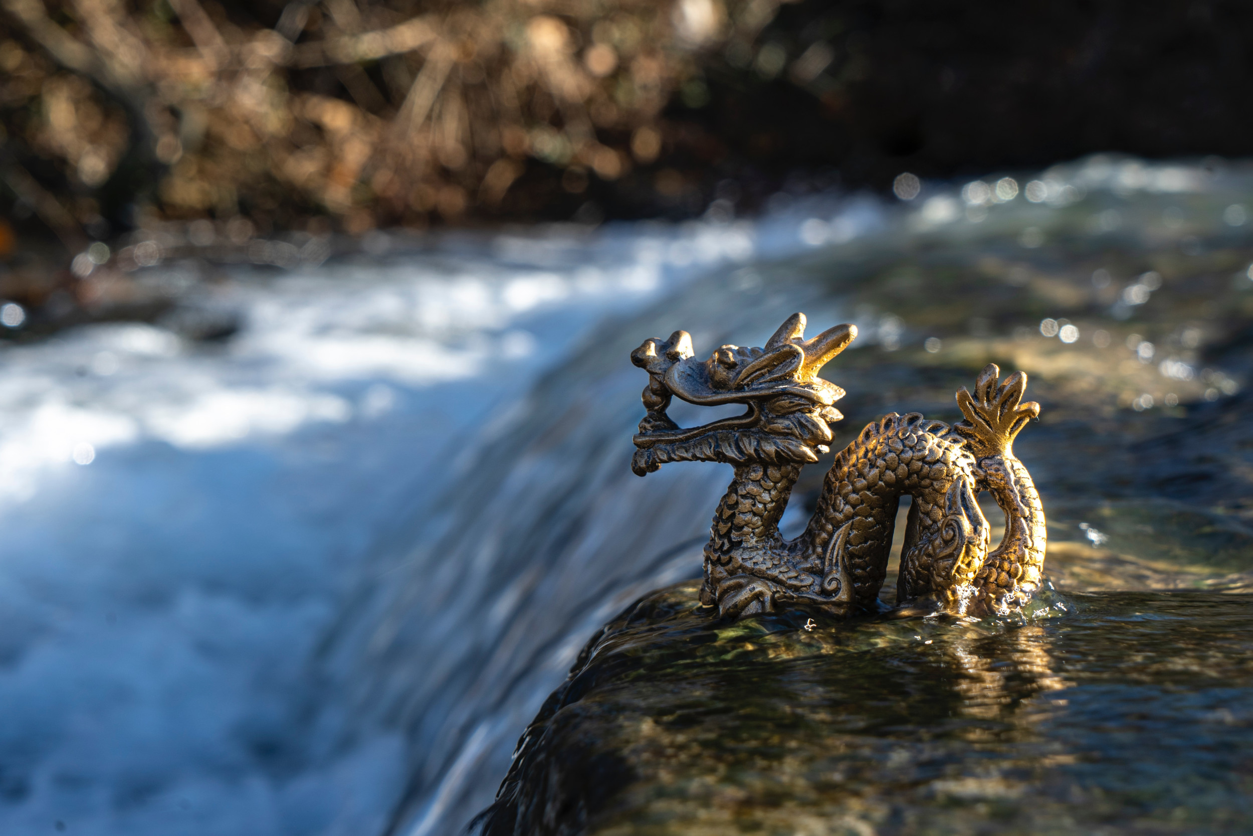 photo of a stone statue of a dragon near a waterfall