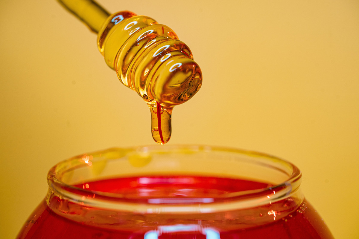 clear glass bottle pouring golden liquid (honey) into clear drinking glass
